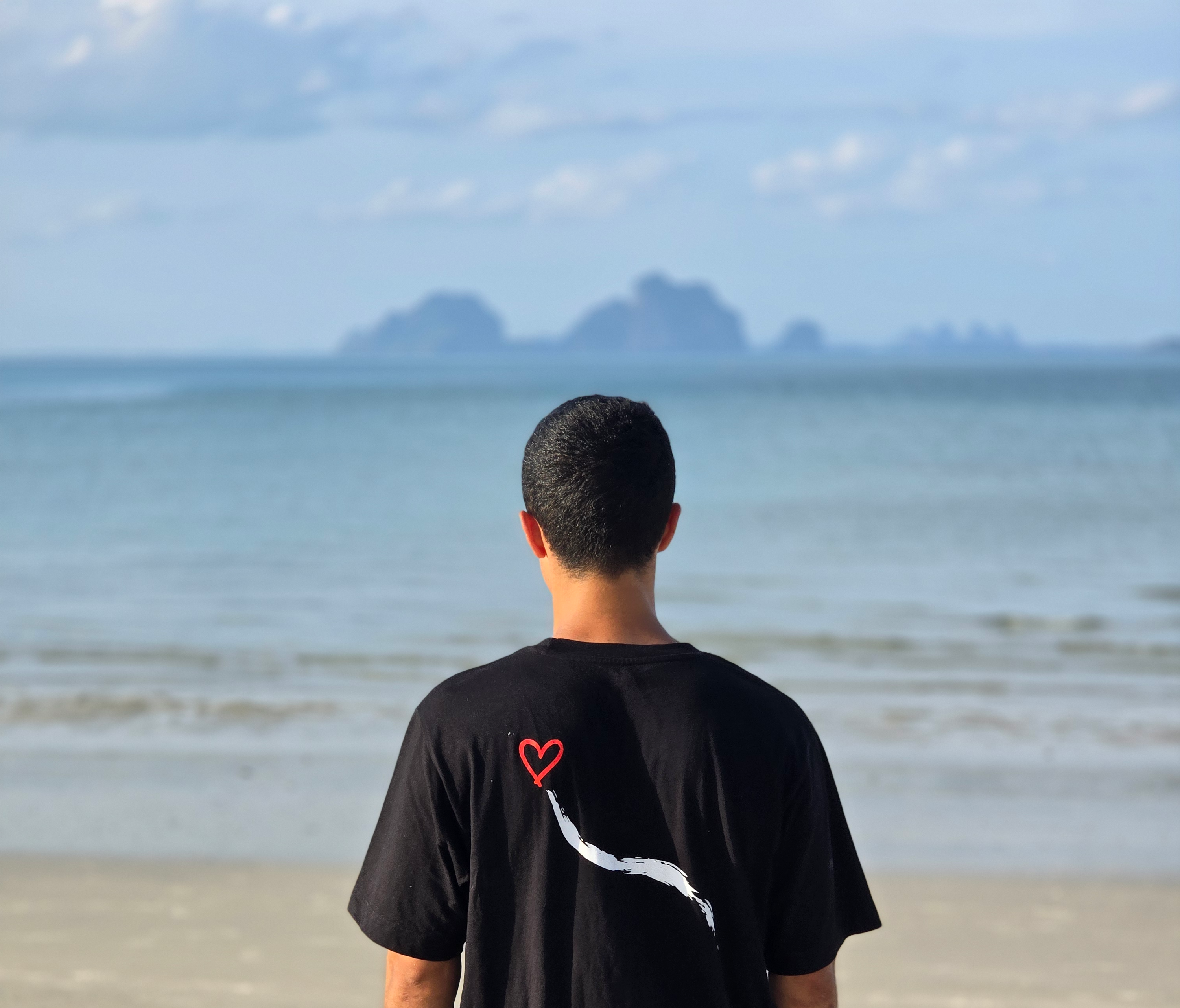 Person wearing a black t-shirt with a red heart design on the beach